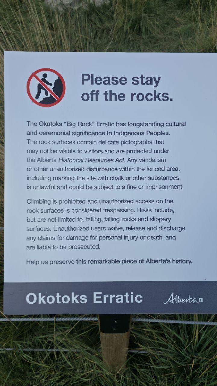 Close-up of the Alberta government sign: 'Please stay off the rocks.' The Okotoks Big Rock Erratic has longstanding cultural and ceremonial significance to Indigenous Peoples. The rock surfaces contain delicate pictographs that may not be visible to visitors... Okotoks Erratic, Alberta.