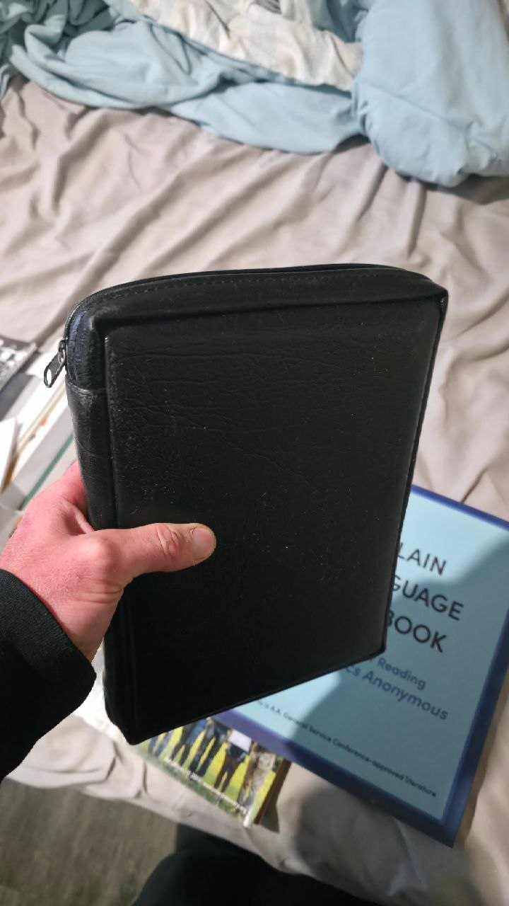 A worn black leather zippered case held in one hand, corners softened and grain polished from years of carry.