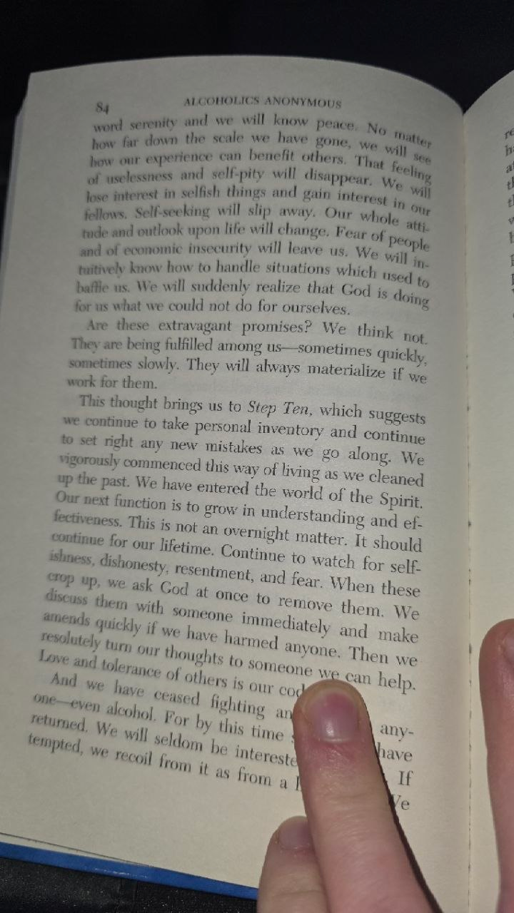 Page 84 photographed at night, a finger resting low on the page over the paragraph beginning 'And we have ceased fighting'; above it the Promises conclude: 'They will always materialize if we work for them.'