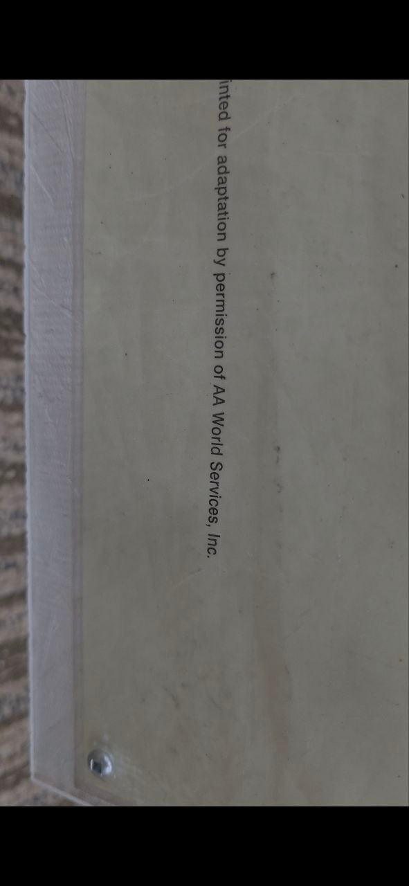 Extreme closeup of the bottom edge of a laminated NA Twelve Traditions poster, a single line of small type: 'printed for adaptation by permission of AA World Services, Inc.'